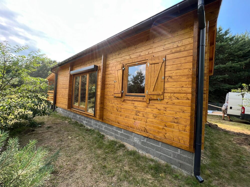 Drewniany dom, z dużymi oknami, ogrodzony trawą.