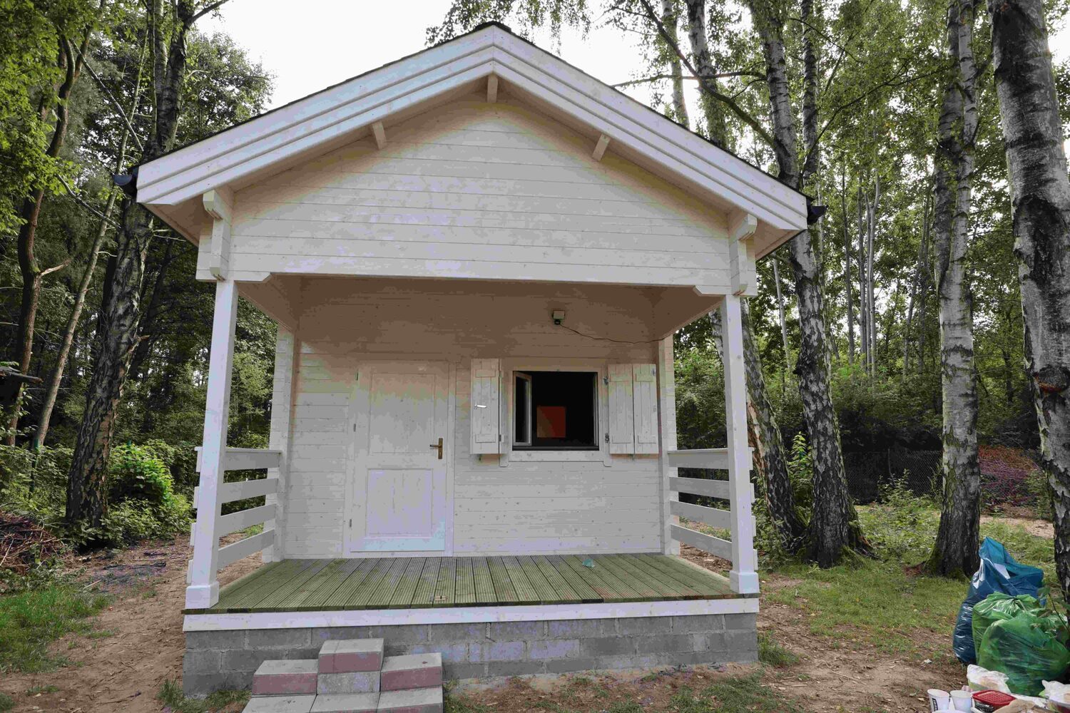 Mały biały domek na drewnianej platformie w lesie.