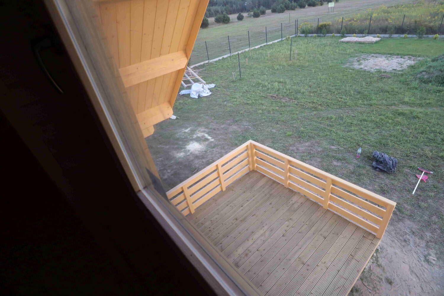 Drewniany taras, zielona trawa, ogrodzenie.