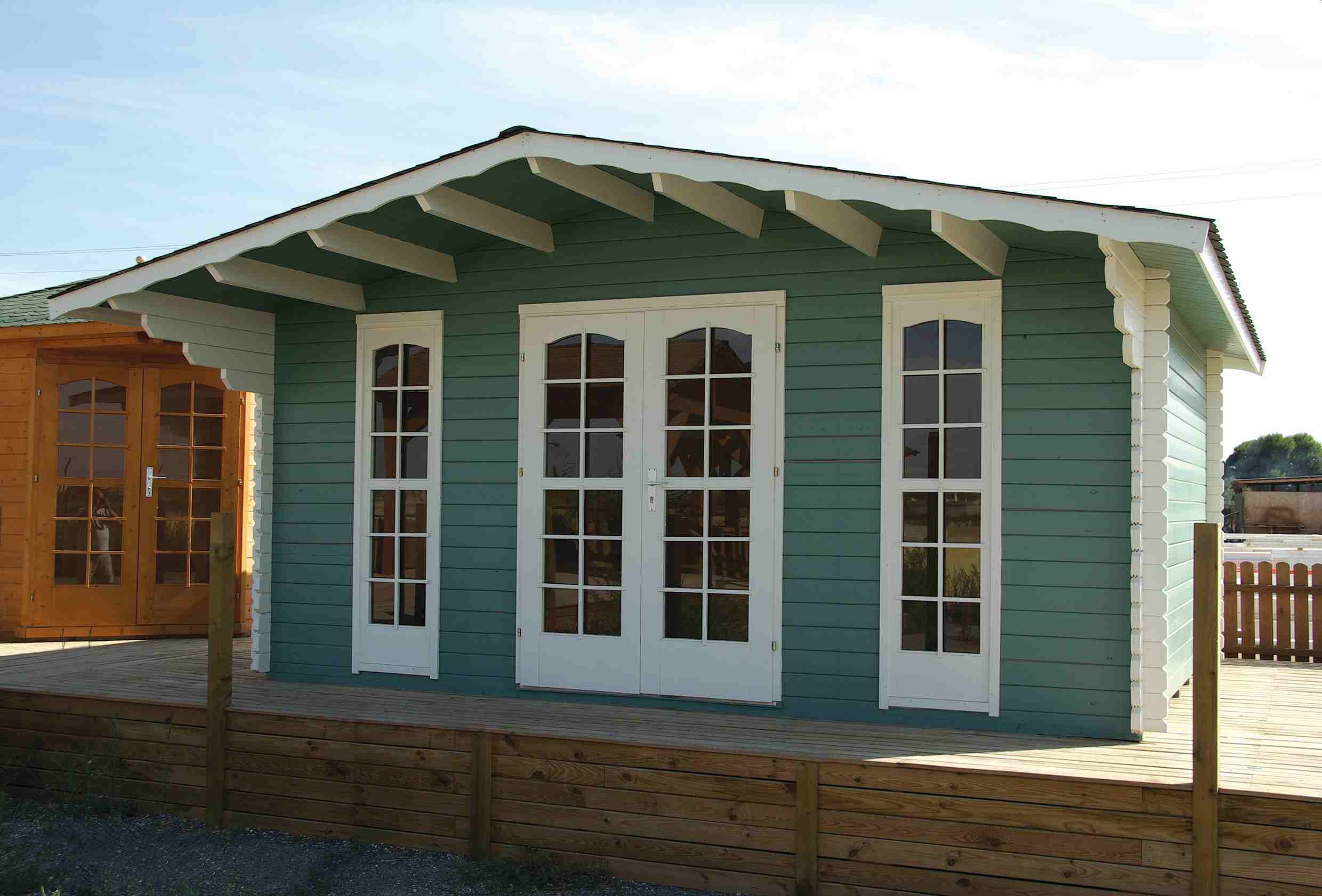 Drewniany domek z zielonymi ścianami i dużymi oknami.