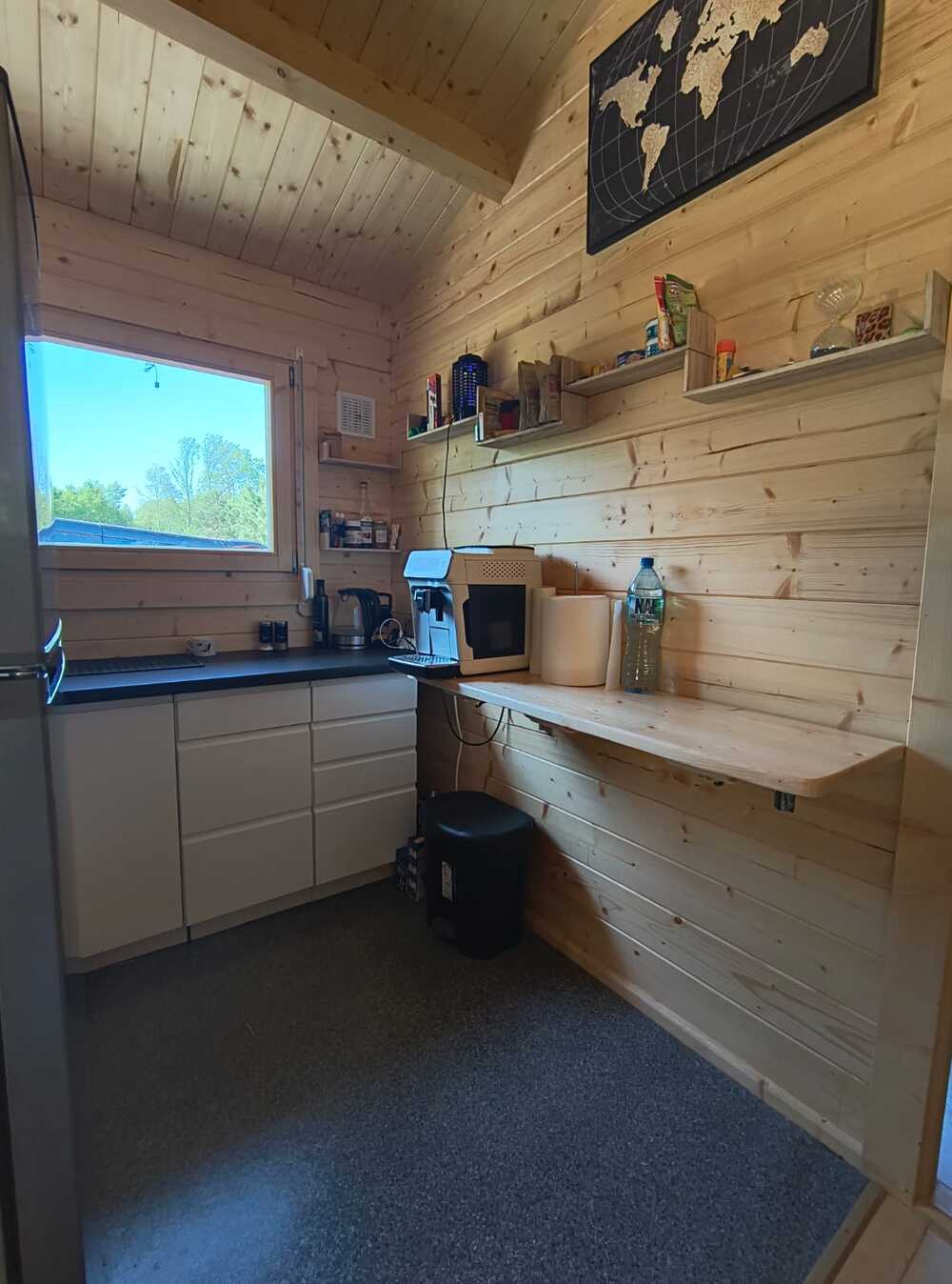 Wnętrze drewnianej kabiny z regałami, oknem i wyposażeniem kuchni.