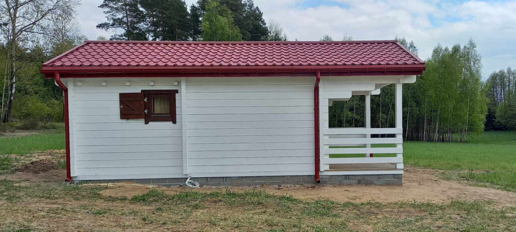Biała drewniana chatka z czerwonym dachem.