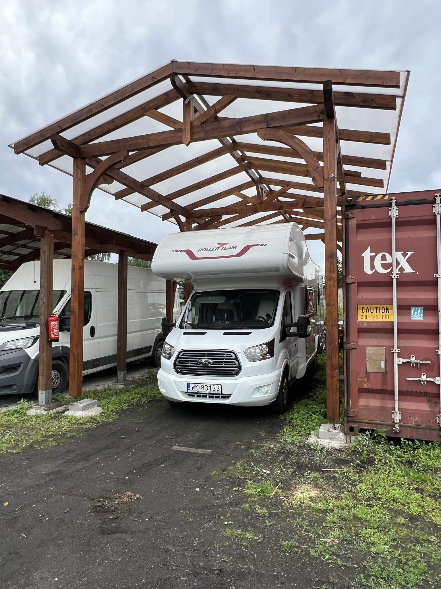 Drewniana wiata, biały kamper, kontener.