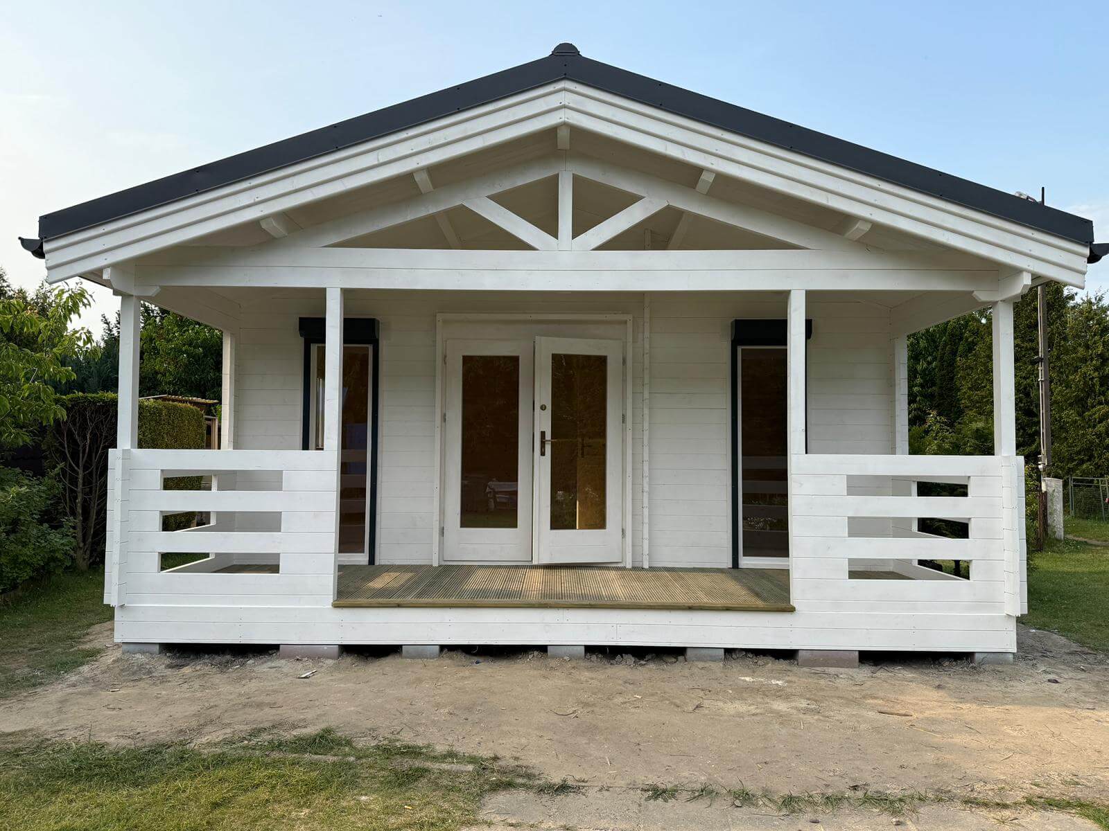 Biały domek z tarasem i dachem dwuspadowym.